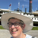 Lisa on vacation in a sun hat with a boat behind her